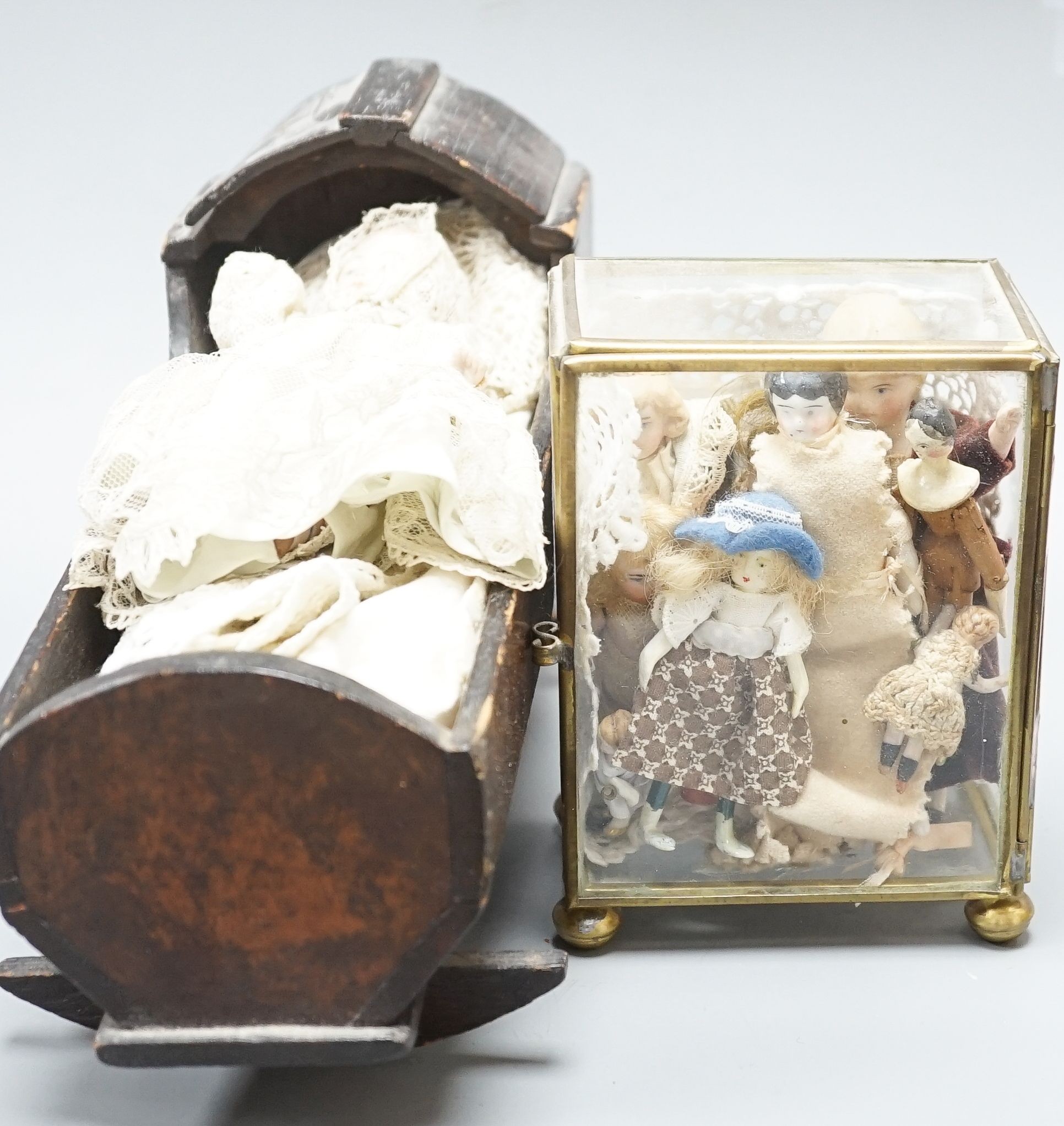 A collection of miniature bisque dolls and another larger doll in a wooden cradle, 11 dolls in total., Cradle 23.5 cms long.